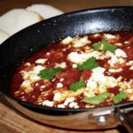 Krewetki smażone w patelni saganaki, a następnie duszone w pomidorach na koniec posypane serem feta i zapiekane.