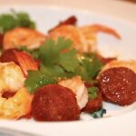 Krewetki smażone z czosnkiem razem z plastrami paprykowanej kiełbasy chorizo podane ze świeżą kolendrą.