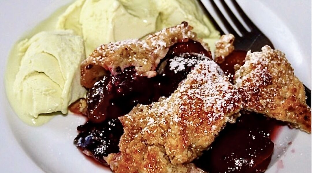 Kruszonka z masła, mąki i bakalii zapiekana ze śliwkami z sokiem z pomarańczy i cynamonem, pieczona i podane z lodami pistacjowymi.