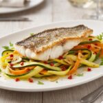 Labraks filet krótko smażony i podany z warzywami w postaci tagliatelle z cukinii i marchewki z dodatkiem czosnku i chili.