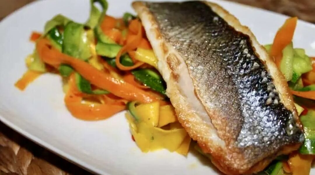 Labraks filet krótko smażony i podany z warzywami w postaci tagliatelle z cukinii i marchewki z dodatkiem czosnku i chili.