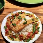 Świeży łosoś pieczony w miodzie, posypany sezamem i podany ze smażonymi warzywami i ryżem.