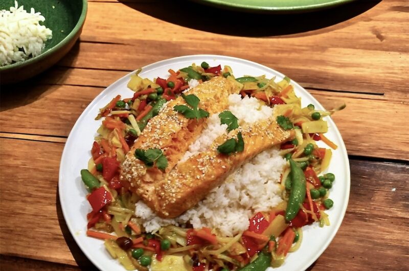 Świeży łosoś pieczony w miodzie, posypany sezamem i podany ze smażonymi warzywami i ryżem.