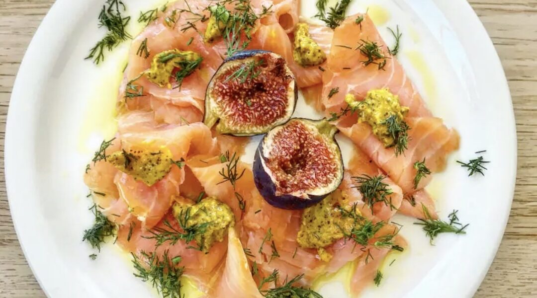 Łosoś wędzony w plastrach podany z dojrzałymi figami i sosem musztardowym, na koniec skropiony oliwą.