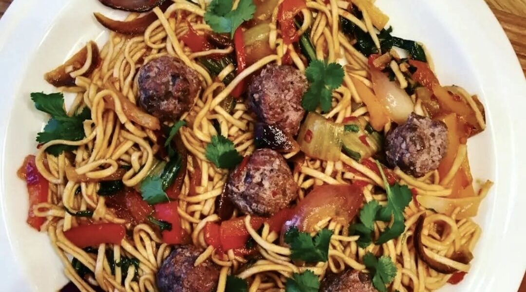 Makaron przyrządzony po chińsku podany z krojonymi i smażone warzywami w ostrym sosie podany z klopsikami jagnięcymi i z dodatkiem świeżej kolendry.