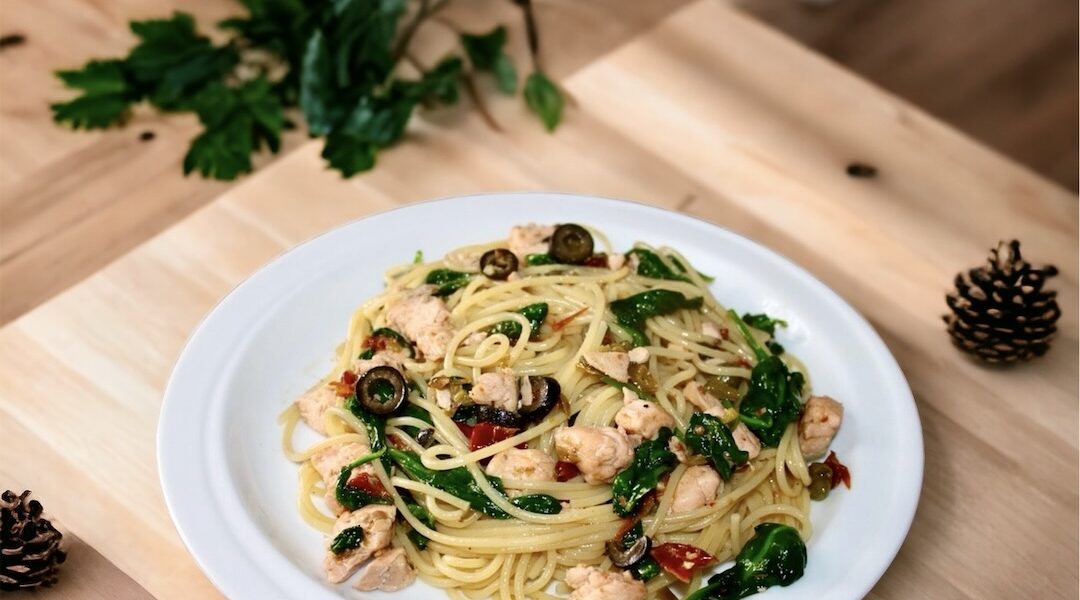 Makaron po hiszpańsku z dodatkiem smażonego łososia, oliwek, suszonych pomidorów i kaparów wzbogacony liśćmi szpinaku.