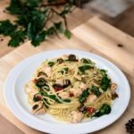 Makaron po hiszpańsku z dodatkiem smażonego łososia, oliwek, suszonych pomidorów i kaparów wzbogacony liśćmi szpinaku.