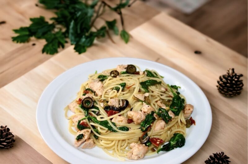 Makaron po hiszpańsku z dodatkiem smażonego łososia, oliwek, suszonych pomidorów i kaparów wzbogacony liśćmi szpinaku.