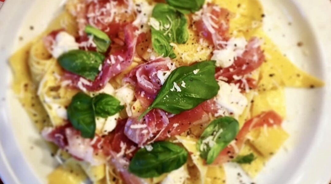 Ugotowany makaron polany oliwą czosnkową i podany z miękkim serkiem, szynką parmeńską oraz listkami bazylii.