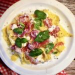 Ugotowany makaron polany oliwą czosnkową i podany z miękkim serkiem, szynką parmeńską oraz listkami bazylii.