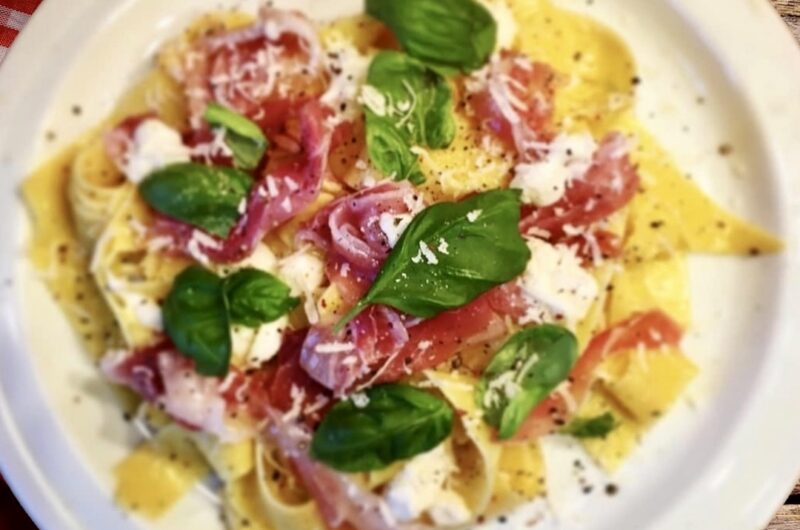 Ugotowany makaron polany oliwą czosnkową i podany z miękkim serkiem, szynką parmeńską oraz listkami bazylii.