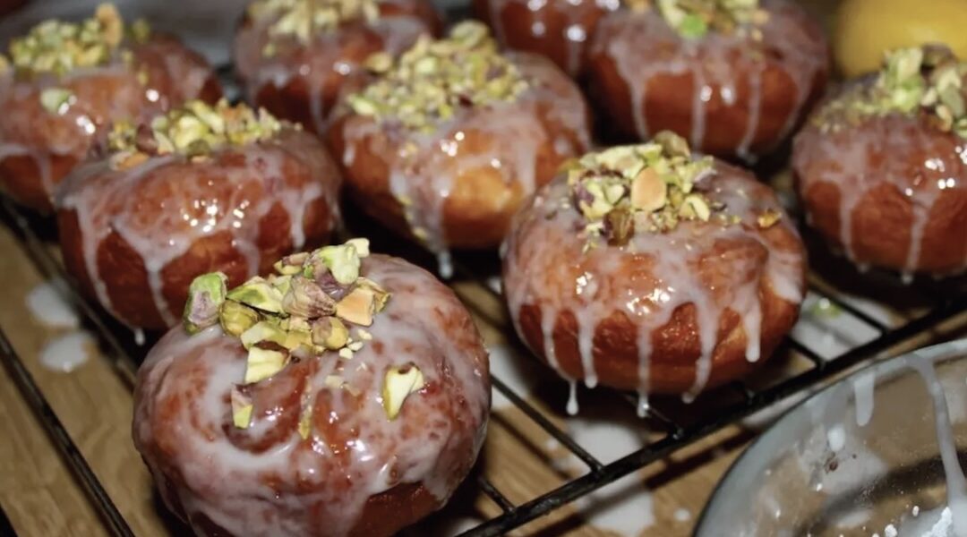 Tradycyjne domowe pączki z ciasta drożdżowego przygotowane z nadzieniem różanym, polane lukrem i posypane startymi pistacjami.