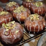 Tradycyjne domowe pączki z ciasta drożdżowego przygotowane z nadzieniem różanym, polane lukrem i posypane startymi pistacjami.