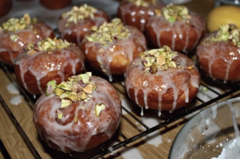 Tradycyjne domowe pączki z ciasta drożdżowego przygotowane z nadzieniem różanym, polane lukrem i posypane startymi pistacjami.