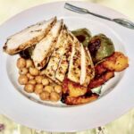 Pierś kurczaka pieczona z warzywami pokrojonymi na kawałki podana z ciecierzycą w sosie z tymiankiem i cytryną.