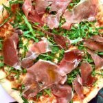 Domowa pizza z pyszną szynką parmeńską i świeżą rukolą.