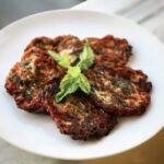 Placki przygotowane ze startych pomidorów Lima z dodatkiem startej cukinii, sera, świeżych ziół i mąki, smażone na patelni tuż przed ich podaniem.