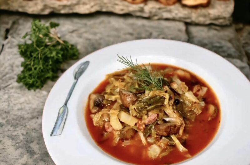 Potrawka z młodej duszonej kapusty z dodatkiem smażonego boczku i grzybów podana w sosie z pomidorów i mielonej papryki.