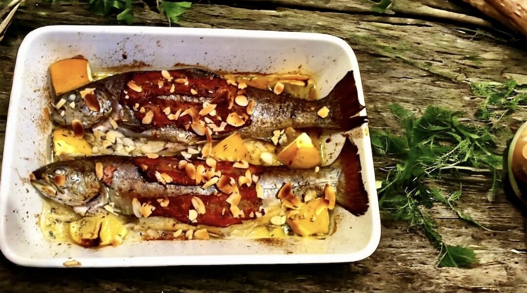 Pstrąg pieczony w całości z kawałkami cytryny oraz z boczkiem i migdałami.