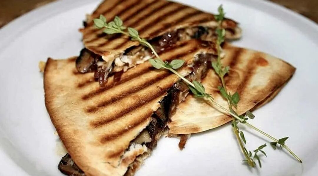 Quesadilla z pieczarkami czyli tortilla obłożona smażonymi pieczarkami, pysznie karmelizowaną cebulą oraz serem, a następnie przykryta drugą tortillą i zapieczona.