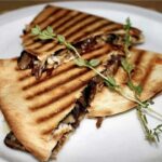 Quesadilla z pieczarkami czyli tortilla obłożona smażonymi pieczarkami, pysznie karmelizowaną cebulą oraz serem, a następnie przykryta drugą tortillą i zapieczona.