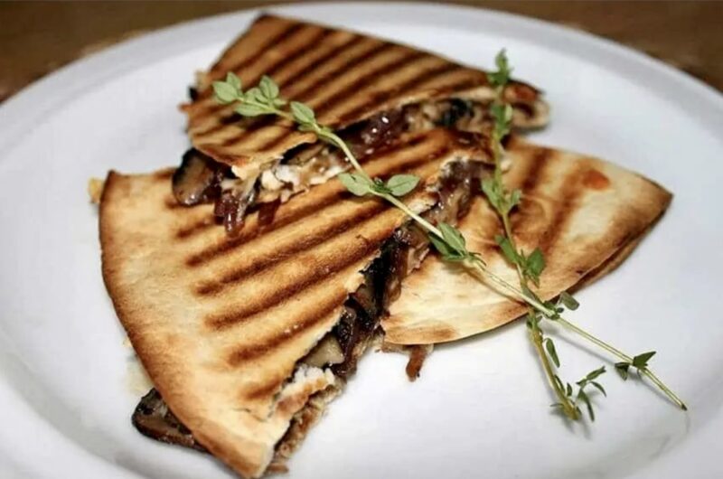 Quesadilla z pieczarkami czyli tortilla obłożona smażonymi pieczarkami, pysznie karmelizowaną cebulą oraz serem, a następnie przykryta drugą tortillą i zapieczona.