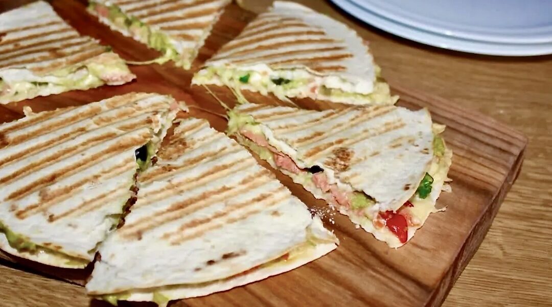 Quesadilla z łososiem to tortilla pokryta puree z awokado podana z łososiem wędzonym, serem i oliwkami a następnie przykryta drugą tortillą i zapieczona.