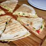 Quesadilla z łososiem to tortilla pokryta puree z awokado podana z łososiem wędzonym, serem i oliwkami a następnie przykryta drugą tortillą i zapieczona.