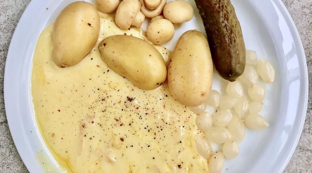 Topiony ser raclette podawany z gotowanymi ziemniakami i kiszonkami.