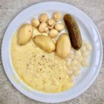 Topiony ser raclette podawany z gotowanymi ziemniakami i kiszonkami.