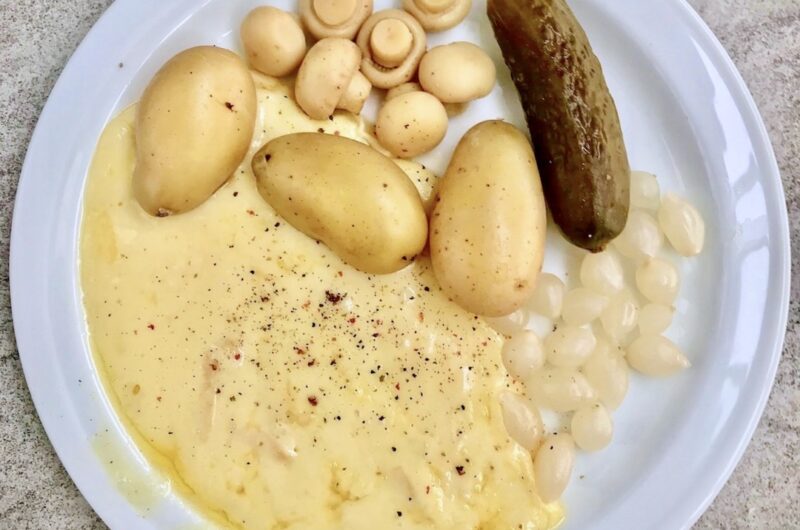 Topiony ser raclette podawany z gotowanymi ziemniakami i kiszonkami.