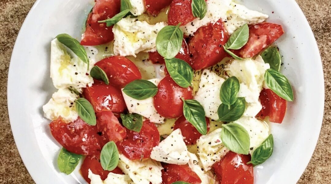 Sałatka caprese to układane na zmianę plasterki albo kawałki pomidorów, mozzarelli oraz listków bazylii, a następnie polane oliwą.