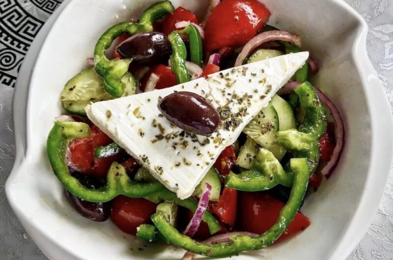 Tradycyjna sałatka grecka z krojonych pomidorów, ogórków, papryki, cebuli  i oliwek podana z plastrem sera feta skropiona oliwą.