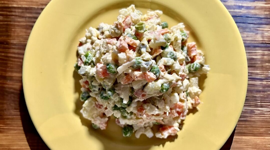 Sałatka jarzynowa z gotowanych i krojonych warzyw korzeniowych z dodatkiem groszku, jajek i ogórków kiszonych połączonych majonezem.