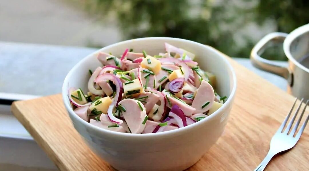 Sałatka szwajcarska z krojonego twardego sera Gruyere, cebuli i kiełbasy parówkowej polana sosem winegret z dodatkiem musztardy.