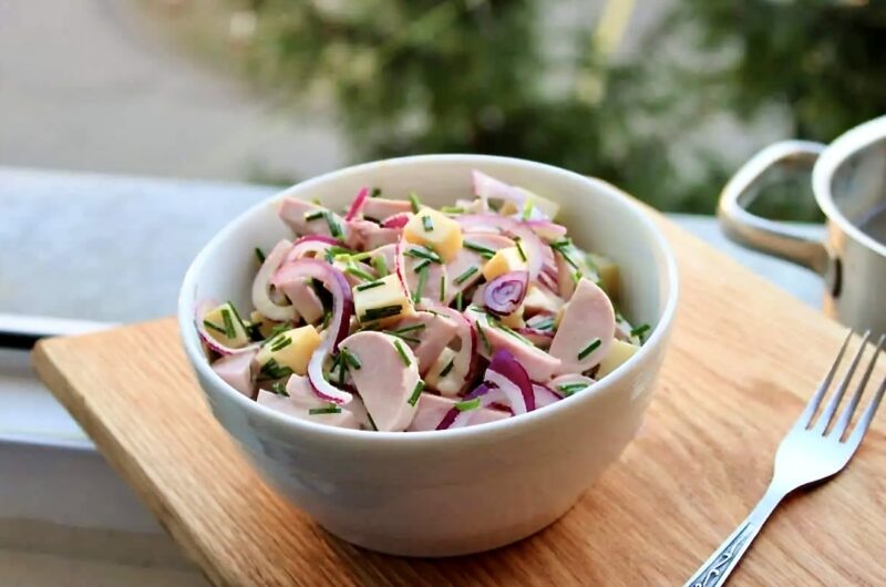 Sałatka szwajcarska z krojonego twardego sera Gruyere, cebuli i kiełbasy parówkowej polana sosem winegret z dodatkiem musztardy.