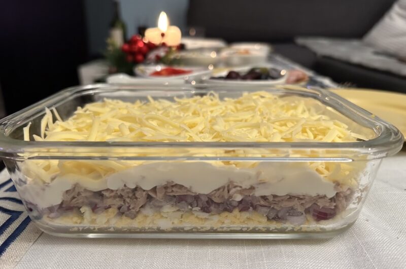 Pyszna sałatka warstwowa z tuńczykiem, startym serem, czerwoną cebulą i gotowanymi jajkami połączonymi majonezem.