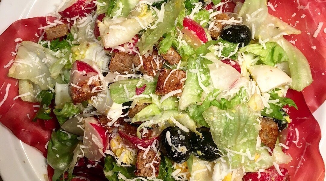 Sałatka z cieniutko pokrojoną w plasterki suszoną wołowiną bresaolą podana z miksem sałat, oliwkami, jajkiem i rzodkiewkami w sosie winegret.