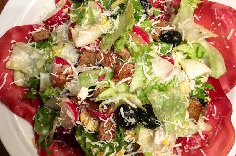 Sałatka z cieniutko pokrojoną w plasterki suszoną wołowiną bresaolą podana z miksem sałat, oliwkami, jajkiem i rzodkiewkami w sosie winegret.