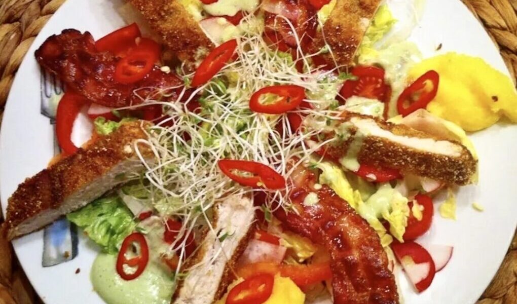 Smakowita sałatka z chrupiącym smażonym kurczakiem, podana z warzywami i polentą oraz z dressingiem o smaku bazylii.