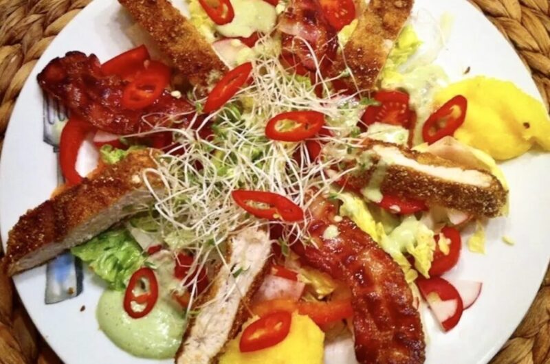 Smakowita sałatka z chrupiącym smażonym kurczakiem, podana z warzywami i polentą oraz z dressingiem o smaku bazylii.