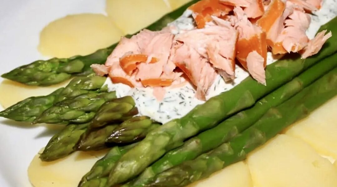 Sałatka z łososiem wędzonym i świeżymi zielonymi szparagami podana na plastrach gotowanych ziemniaków polana sosem koperkowym.