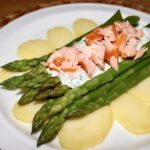 Sałatka z łososiem wędzonym i świeżymi zielonymi szparagami podana na plastrach gotowanych ziemniaków polana sosem koperkowym.