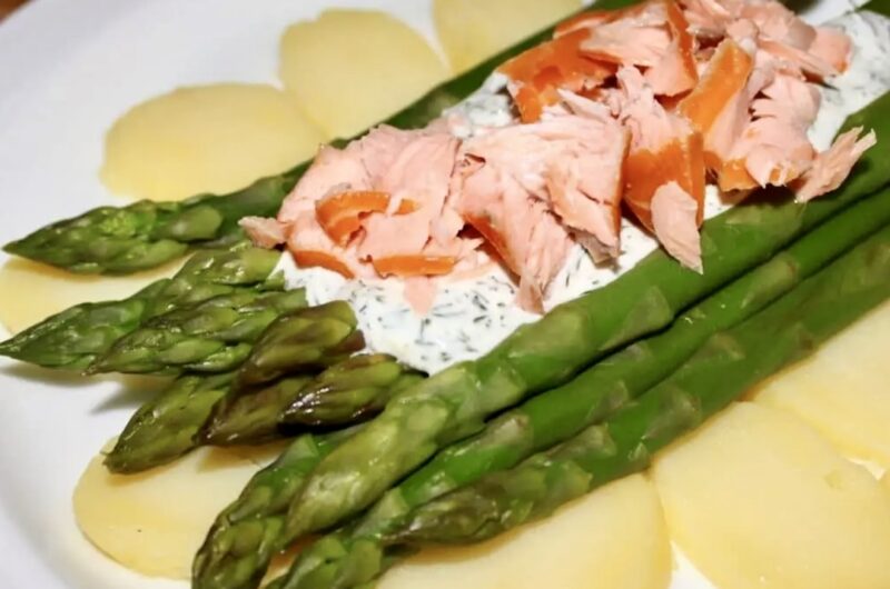 Sałatka z łososiem wędzonym i świeżymi zielonymi szparagami podana na plastrach gotowanych ziemniaków polana sosem koperkowym.