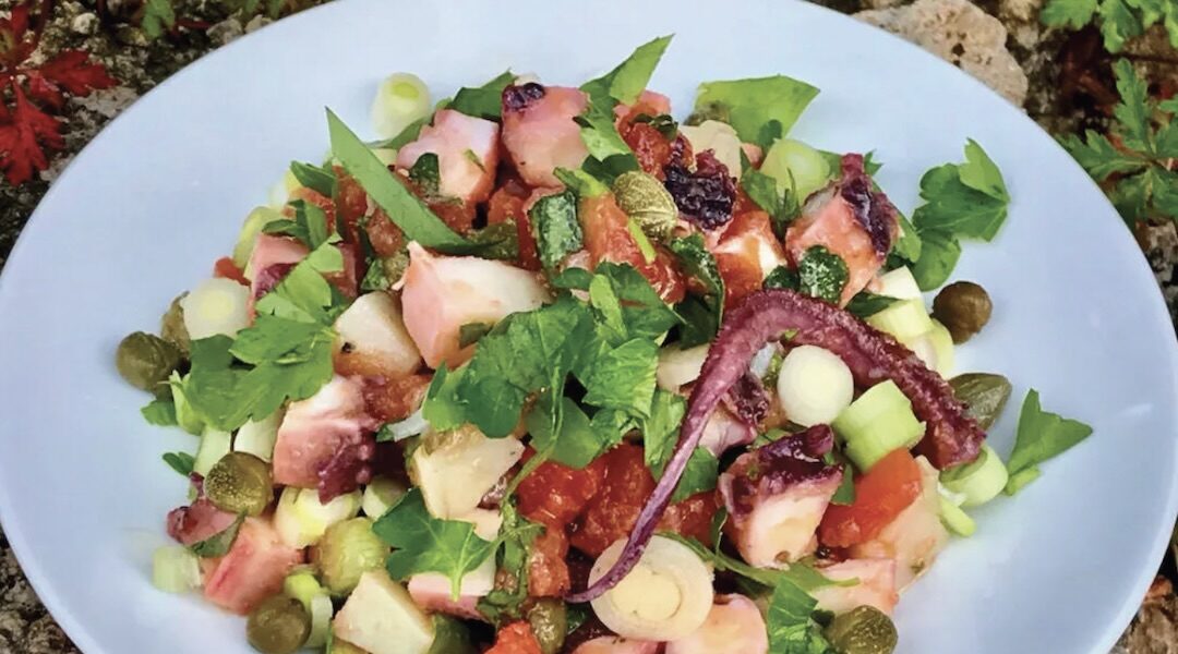 Sałatka z ugotowaną i pokrojoną ośmiornicą z dodatkiem cebuli, pomidorów oraz ziemniaka skropiona sosem winegret.