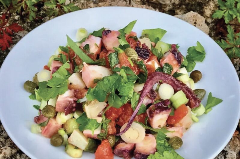 Sałatka z ugotowaną i pokrojoną ośmiornicą z dodatkiem cebuli, pomidorów oraz ziemniaka skropiona sosem winegret.