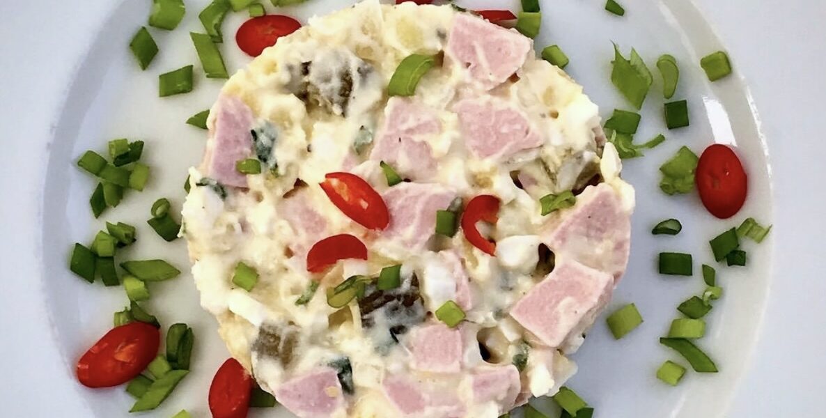 Sałatka z ziemniaczana z jajkami, kiełbasą parówkową i ogórkiem kiszonym połączonymi majonezem.