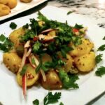 Sałatka ziemniaczana przygotowana z ugotowanych ziemniaków pokrojonych na duże kawałki zmieszanych z rzodkiewkami, kaparami i korniszonami podana z sosem musztardowym.