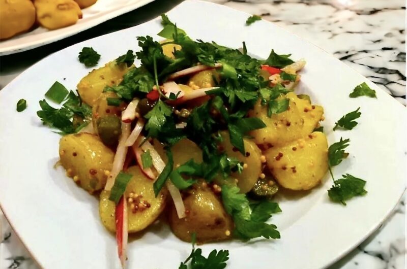 Sałatka ziemniaczana przygotowana z ugotowanych ziemniaków pokrojonych na duże kawałki zmieszanych z rzodkiewkami, kaparami i korniszonami podana z sosem musztardowym.