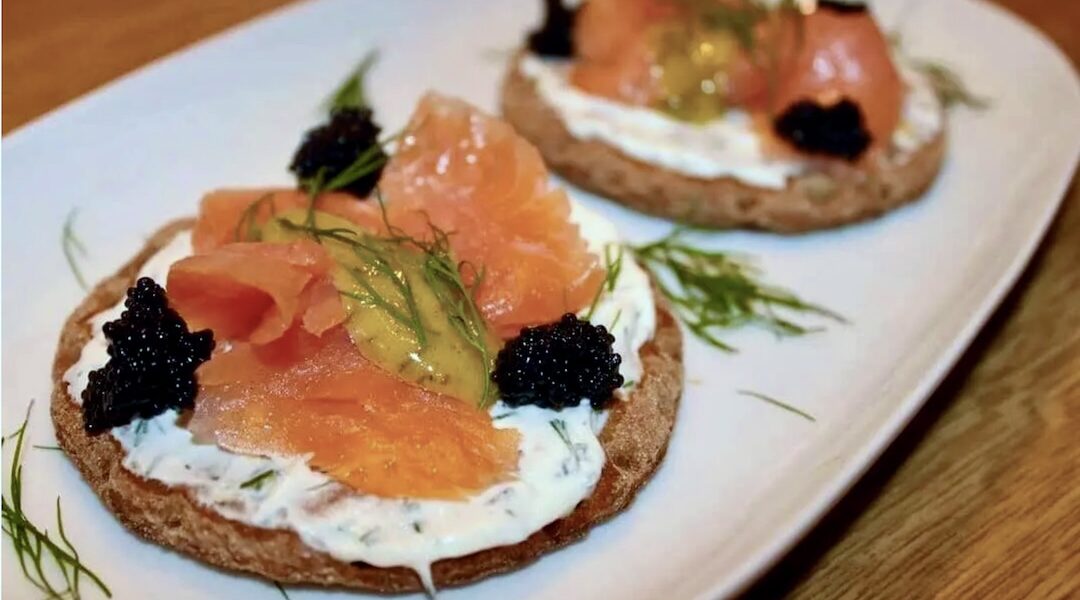 Kanapki szwedzkie przygotowane z sucharków posmarowanych serkiem i obłożonych łososiem wędzonym podane z sosem musztardowym z koperkiem.